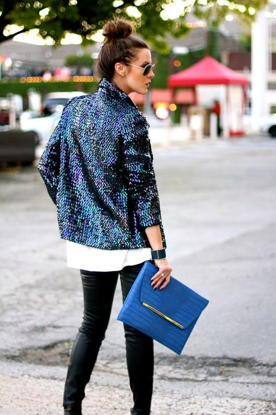 Moça de costas com blazer de paetê calça de couro e bolsa azul