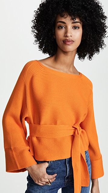 blusa laranja de tricô levemente estruturado com mangas sino e amarração na cintura, usada por modelo negra de cabelos encaracolados médios.